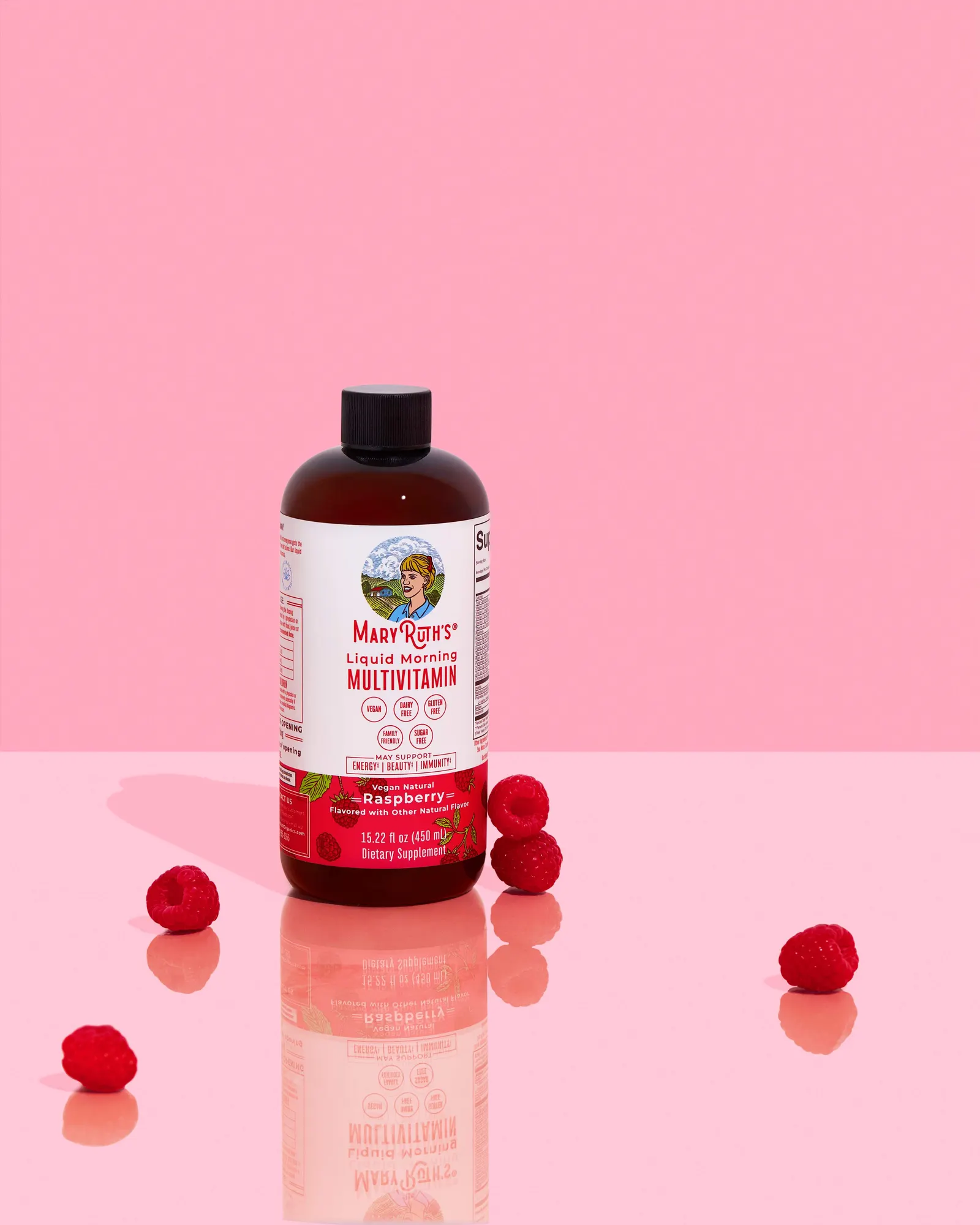 MaryRuth&rsquo;s Raspberry Liquid Morning Multivitamin on a glossy pink set with fresh raspberries and a soft reflection